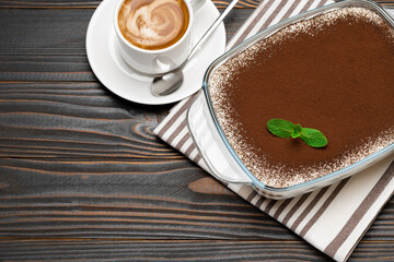 Traditional Italian Tiramisu dessert in glass baking dish and cup of fresh hot espresso coffee on wooden background