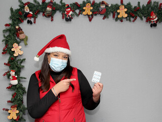 
Latin woman with protection mask, hat and medicine for illness in Christmas decoration, new normal...