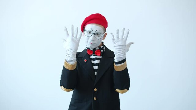 Happy mime with expressive face is dancing and gesturing against white background having fun moving arms and fingers wearing funny costume