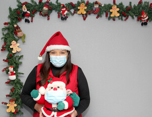 Latin woman with protection mask, hat and Santa Claus doll in Christmas decoration, new normal...
