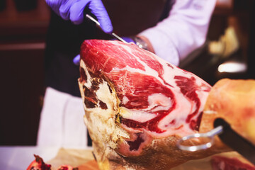 A process of slicing Hamon Jamon, traditional spanish ham on a wooden stand, slices of Parma Ham, as a part of catering on corporate party event or wedding celebration