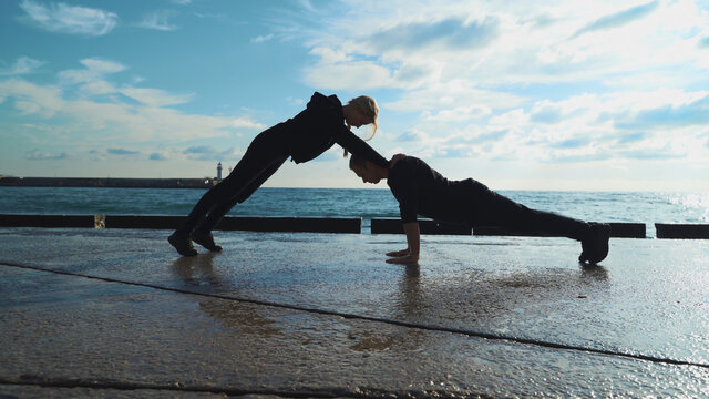 Young couple in sportswear are engaged in morning exercises against the background of the sea. The guy and the girl go in for sports together.