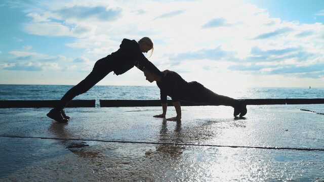 Young couple in sportswear are engaged in morning exercises against the background of the sea. The guy and the girl go in for sports together.