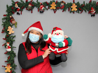 Latin woman with protection mask, hat and Santa Claus doll in Christmas decoration, new normal...