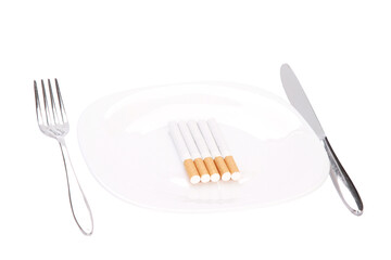 High angle shot of cigarettes on a plate with a knife and a fork on a white surface
