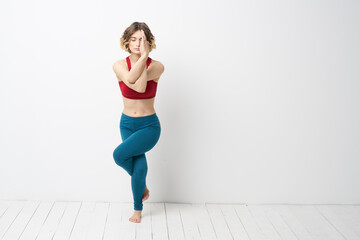 Fototapeta na wymiar sports woman in a bright room doing yoga in full growth blue leggings and a red tank top