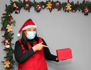 
Latin woman with protection mask, santa claus hat and gift box in Christmas decoration, new normal...