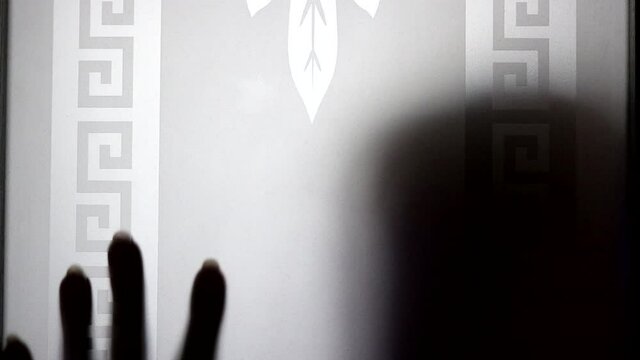 A vague woman's hand drops behind frosted glass. A shadow from the head is visible. Violence, loneliness, horror concept. Video in polychrome colors. Blurred vintage frame.