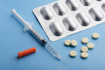 a syringe with a vaccine and pills on a blue background. syringe with antibiotic pills on a blue...