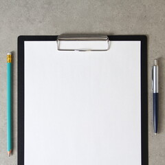 Template of white paper with a ballpoint pen and simple pencil on light grey concrete background in a black tablet with a clip. Concept of new idea, business plan and strategy. empty space for text