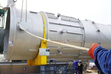 Worker during rope access rigger commencing high risk job to holding a safety tag line rope to control a load while crane, boom truck, truck loader is lifting transformers unit in chemical plant.