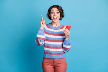 Photo of charming girl hold cellphone raise finger up open mouth wear striped sweater red pants isolated blue color background