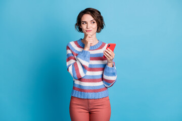 Photo of pretty girl hold cell phone finger chin look side empty space wear striped pullover red...