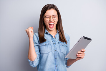 Fototapeta premium Photo of impressed hooray long hairdo girl hand fist yell hold tablet closed eyes wear spectacles blue cloth isolated on grey background