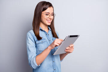 Profile portrait of optimistic cute long hairdo girl writing tablet wear spectacles blue cloth isolated on grey background