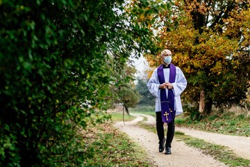 Priest in the medical mask is walking through the village.