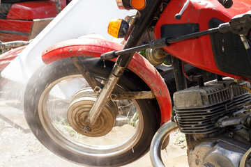 Washing the motorcycle with a strong jet of water. Motorcycle wheel close up.