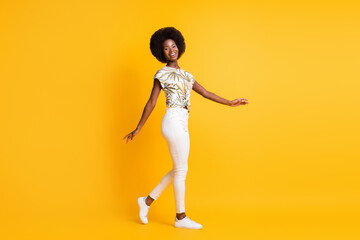 Fototapeta na wymiar Full size profile photo of optimistic nice curly hair lady walking dress bright t-shirt sneakers trousers isolated on yellow background