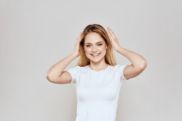 Fototapeta na wymiar cheerful blonde in a white t-shirt gesturing with her hands light background