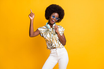 Photo of trend cheerful curly hair lady dancing wear headphones spectacles t-shirt trousers isolated over yellow color background