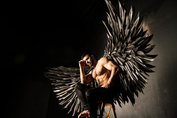 handsome athletic man in black angel costume on black background