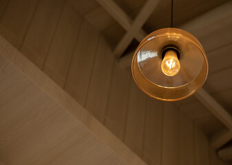 selective focus and up view shot with copy space of vintage ceiling lamp hung on wooden ceiling with light bulb shows shining yellow light in antique style restaurant giving calm and peace mood