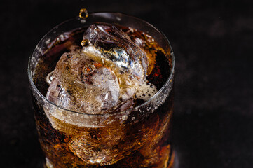 refreshing drink, cold soda with ice cubes in a glass on a black background
