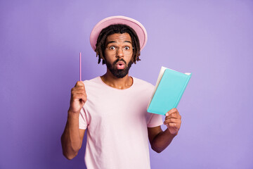 Photo of young afro amazed surprised handsome man male guy point pen in copyspace hold blue diary isolated on violet color background