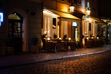 Fototapeta na wymiar Cafe tables and chairs outside in old cozy street in in Prague. Christmas holidays and travel. Christmas decorations lights.