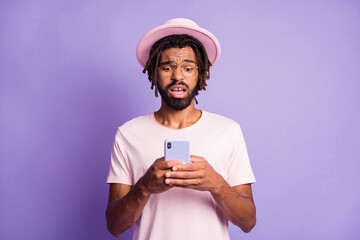 Photo portrait of upset guy holding phone in two hands isolated on vivid violet colored background