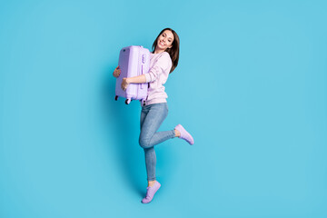 Full length photo of positive girl hug her suitcase enjoy travel tour borders open wear lilac violet pullover sneakers isolated over blue color background