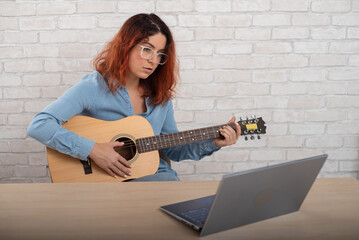 Caucasian woman learning to play guitar online. The girl sits in quarantine remotely studying music