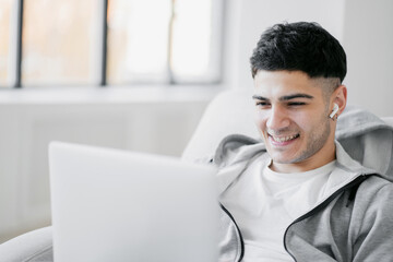 talks to friends via online communication in a social community. Looking at a laptop computer a dark haired man smiles enjoys communicating with loved ones