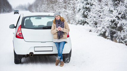 Woman with smartphone standing next the car on a background of snow-covered winter forest