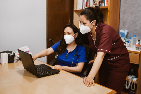 Woman Doctor And Mexican Nurse Wearing Facial Mask And Checking Laptop Information In Mexico