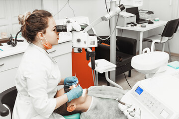 Dentist young woman treats a patient a man. The doctor uses disposable gloves, a mask and a hat. The dentist works in the patient's mouth, uses a professional tool.