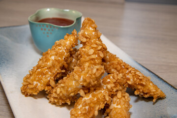 A plate of crispy chicken strips made from Rice Krispies Multigrain Cereal deep fried with a bowl of tomato source