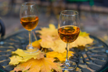 Two glasses of cognac-colored white wine on the outside on a table covered with yellow leaves.
