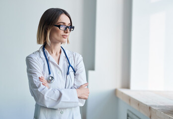 doctor woman in a medical gown with a stethoscope in glasses looks out the window