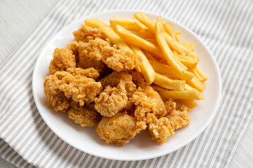 Homemade Fried Chicken Bites and French Fries on a plate, side view.