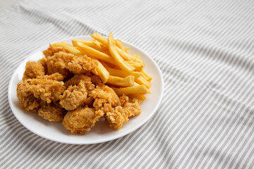 Homemade Fried Chicken Bites and French Fries on a plate, side view. Space for text.
