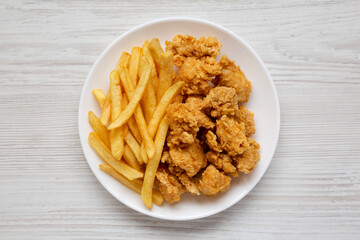 Homemade Fried Chicken Bites and French Fries on a plate on a white wooden table, overhead view. Flat lay, top view, from above.