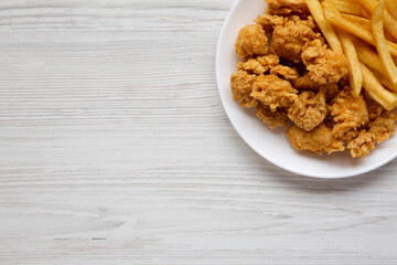 Homemade Fried Chicken Bites and French Fries on a plate on a white wooden background, overhead view. Flat lay, top view, from above. Copy space.