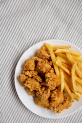 Homemade Fried Chicken Bites and French Fries on a plate on cloth, overhead view. Flat lay, top view, from above. Copy space.