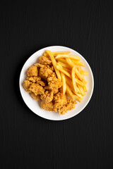 Homemade Fried Chicken Bites and French Fries on a plate on a black background, top view. Flat lay, overhead, from above.