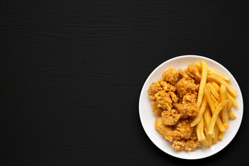 Homemade Fried Chicken Bites and French Fries on a plate on a black background, overhead view. Flat lay, top view, from above. Space for text.