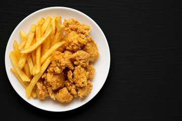 Homemade Fried Chicken Bites and French Fries on a plate on a black surface, overhead view. Flat lay, top view, from above. Space for text.