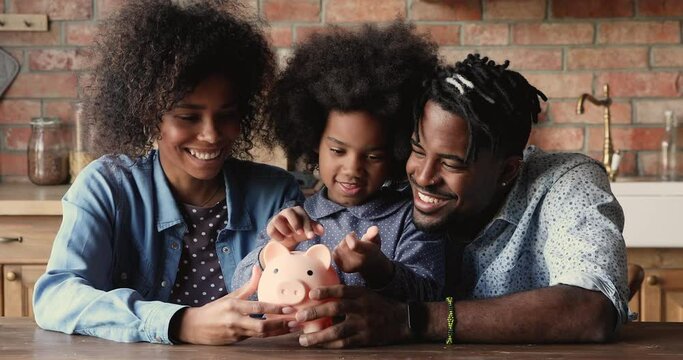 African family with little daughter sit at table in kitchen, preschool 6s girl counts, puts coins in piggy bank, parents teaches child save money, think about future, manage personal savings concept