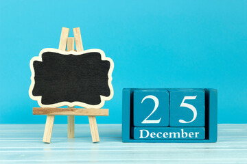 wooden calendar with the date of December 25 and an easel on a blue background, place for text