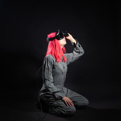Fototapeta na wymiar young woman with pink hair and in a jumpsuit uses virtual reality glasses, is in the game,